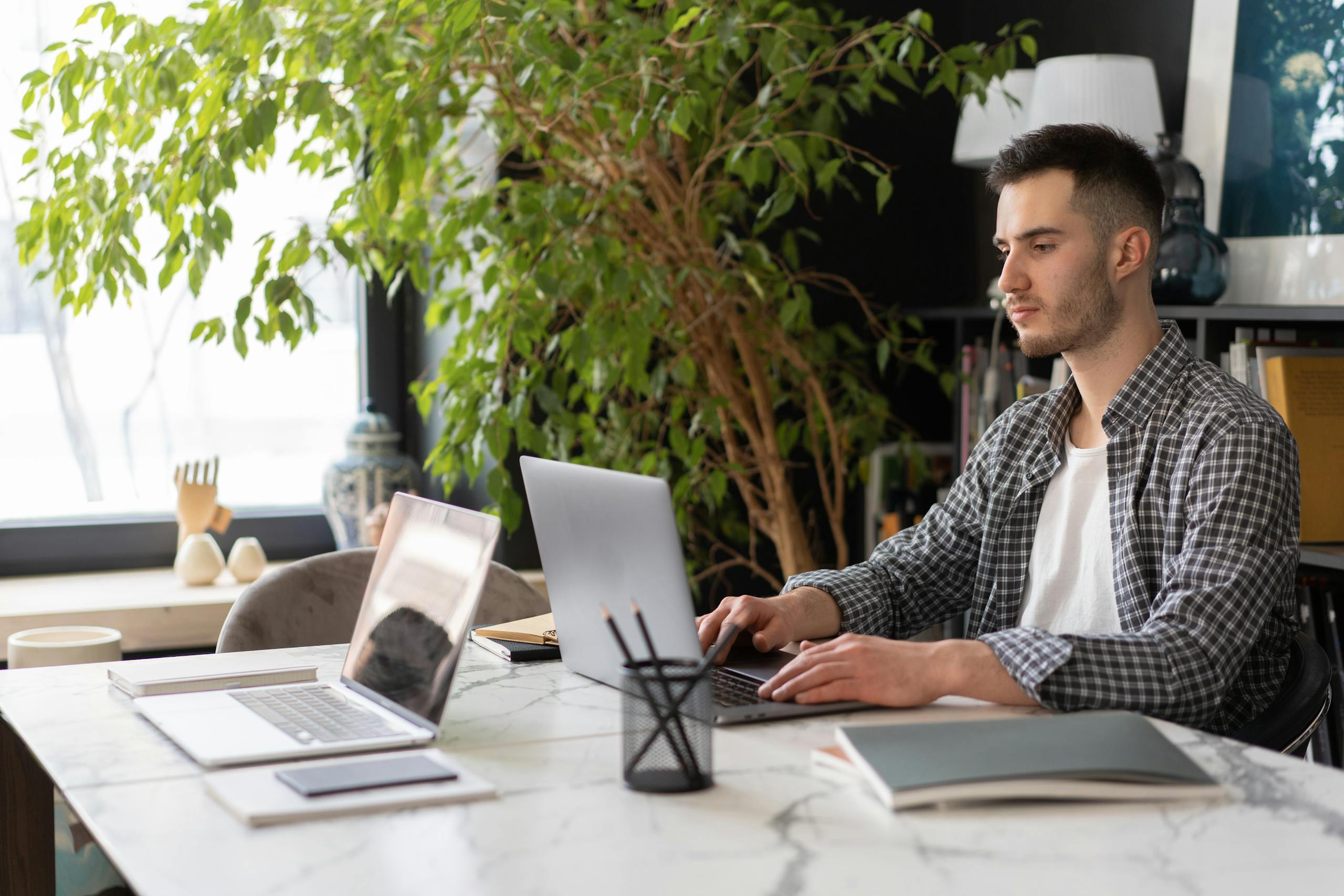 Young man working on a laptop in a stylish indoor office setting with greenery.